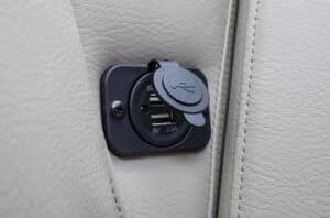 Close-up of a dual USB charger socket embedded in a light-colored leather surface, likely part of a car interior. The socket is covered with a protective cap and marked with “5V 2.4A” indicating the output voltage and current.