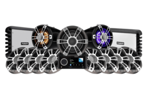 A display of Fusion-branded audio equipment, featuring multiple speakers, subwoofers, and amplifiers arranged symmetrically. The central subwoofer is flanked by speakers with illuminated lights. A control unit with a digital screen is placed in the front.