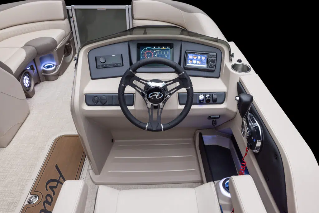 The driver's console of a modern boat featuring a steering wheel, various controls, a touchscreen display, and instrument gauges. The interior has beige seats, cup holders, and LED lighting accents. The boat floor is equipped with non-slip mats.