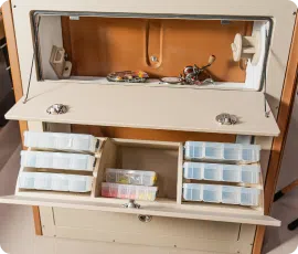 A crafting workstation with an open storage compartment. Various small plastic containers, perfect for organizing beads or screws, are neatly arranged. Wires and tools are scattered around the workstation, reminiscent of pontoons near me that bring a sense of organized chaos.