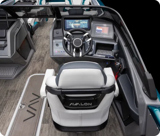 A sleek and modern boat cockpit with a white captain's seat featuring the brand name "Avalon," available through your local pontoons dealer. The dashboard includes a steering wheel, multiple screens displaying navigation and control information, and various control buttons. The floor is covered in a textured material.