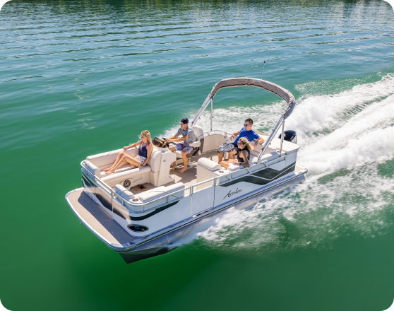 A motorboat cruises on clear green water, carrying four people under a partially shaded canopy. Two sit at the front, one at the helm, and one at the back. The boat leaves a wake behind as it speeds forward, illustrating a sunny day on the water—the perfect scene to inspire anyone to buy pontoons.