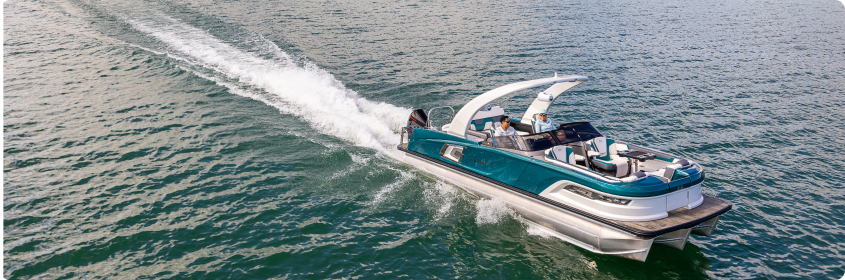 A sleek, modern motorboat with a white hull and teal accents speeds across a calm body of water, creating a white wake behind it. Several people are on board, enjoying the ride under a clear, sunny sky. Experience this joy when you buy pontoons to elevate your time on the water.