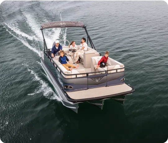 A pontoon boat glides through the water with five people on board. The group, consisting of four adults and one child, appears relaxed and enjoys the ride. The boat, supported by sturdy aluminum pontoons, has a canopy, cushioned seats, and a spacious deck, surrounded by calm waters.