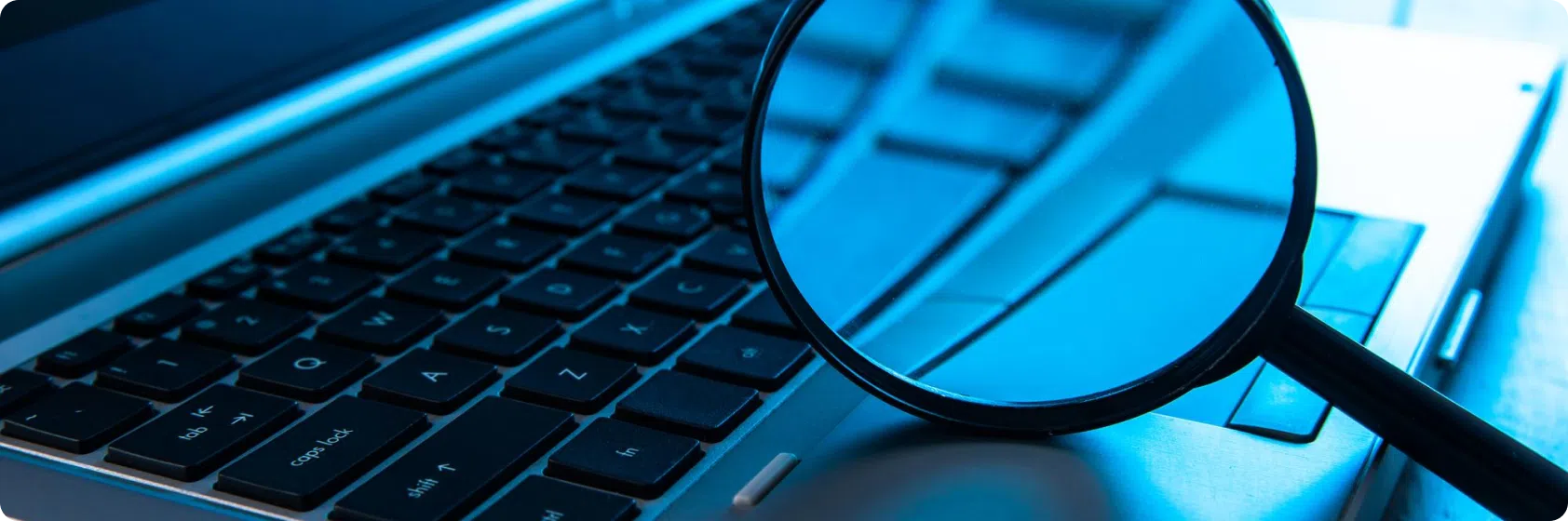 A close-up image of a magnifying glass held over a laptop keyboard, providing a detailed look at a few keys while the background remains slightly blurred. The predominantly blue color tone creates a cool and focused atmosphere, akin to closely examining pontoon boat prices for precise details.