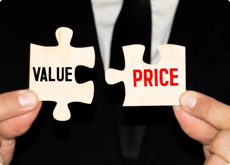 Close-up of hands holding two puzzle pieces in front of a person wearing a suit. The piece in the left hand has the word "VALUE" in black, and the piece in the right hand has the word "PRICE" in red, suggesting the connection between value and price, much like new pontoon boat sales.