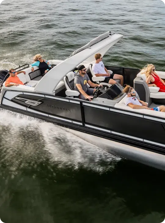 A motorboat, comparable to the cost of a pontoon boat, speeds across the water with six people on board. Two individuals are at the helm, navigating, while the others relax. The boat creates a wake as it moves through the water.