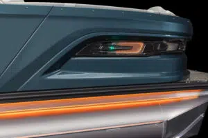 Close-up of a sleek, modern boat with dark blue exterior and illuminated, orange and green LED lights near the stern. The hull features metallic accents and a futuristic design.