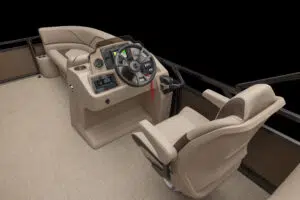 View of a boat's helm with a beige captain's chair, steering wheel, and various controls on the console. The seating is upholstered in light tan fabric, and the floor is carpeted. The background is a solid black.