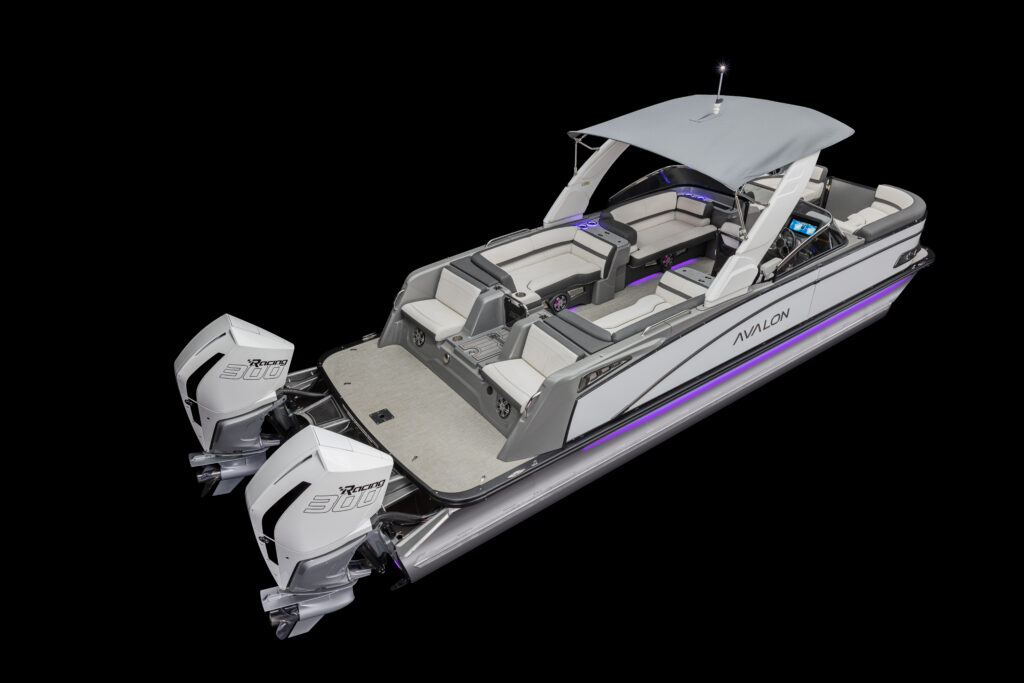 A silver pontoon boat with two large outboard motors, showing spacious seating, a canopy, and a sleek, modern design against a black background. The interior is furnished with light gray and purple accents.