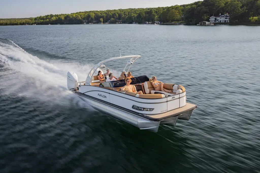 The Catalina Cruise Rear Bench Windshield glides swiftly across the lake, carrying five passengers who savor the ride under a sunny sky. The boat leaves a wake in the water with trees lining the shore in the distance.