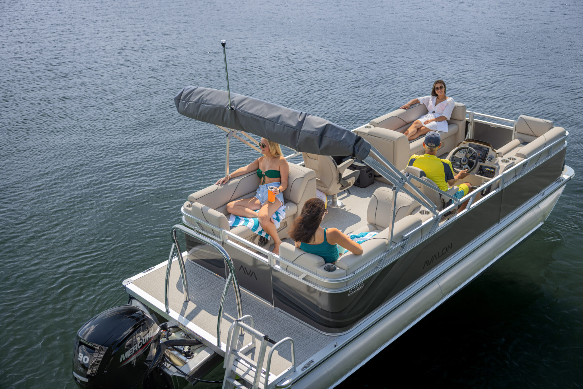 A group of four people relaxes on a pontoon boat in the middle of a calm lake. The boat has a canopy and comfortable seating. One person steers, while others enjoy drinks and conversation under the sun.