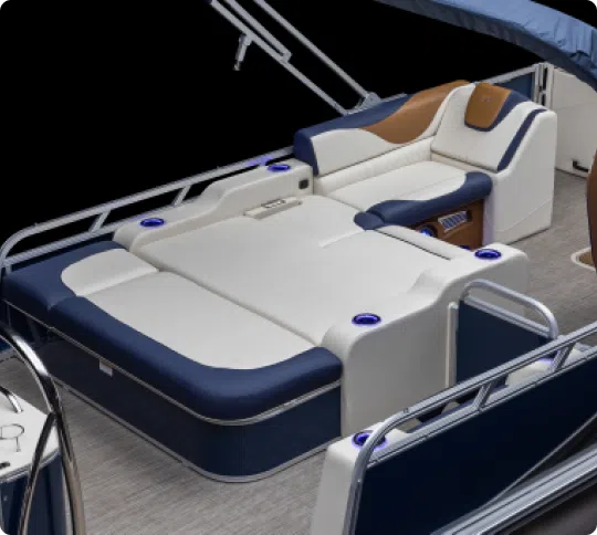 A standout among pontoon boat brands, this model boasts a sleek interior with cushioned navy and white seating, reclining lounge areas, and metallic railing.