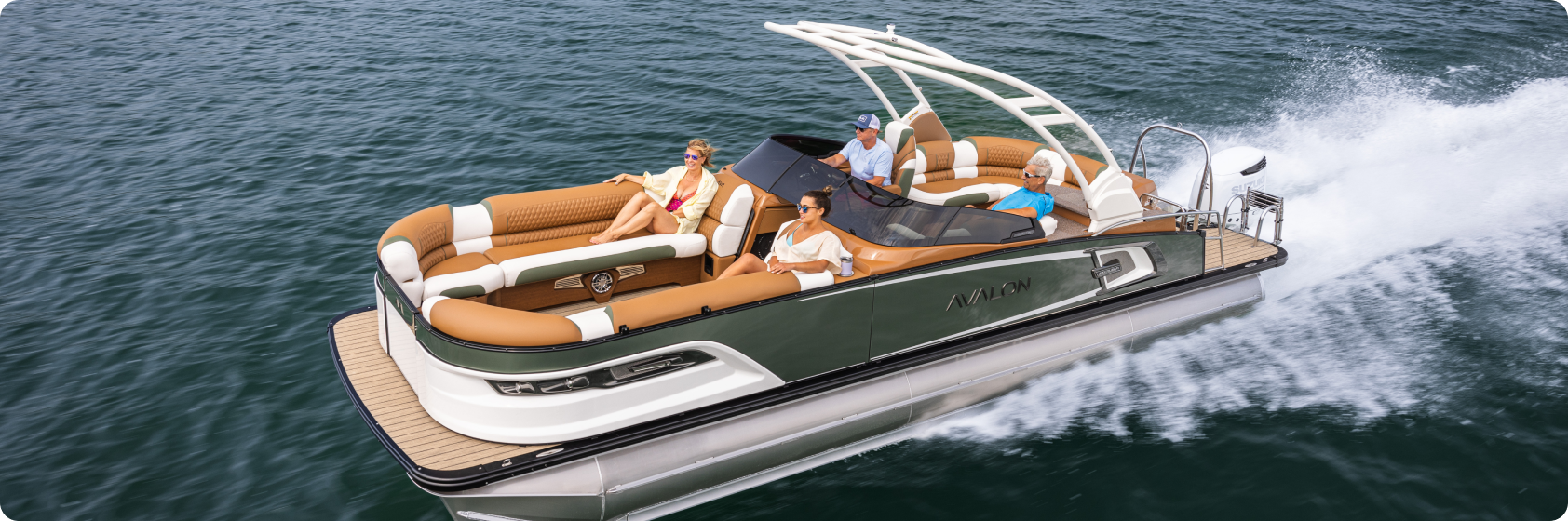 A group of people enjoying a sunny day on a sleek pontoon boat cruising over calm water, with comfortable seating featuring tan and white upholstery and a sturdy table perfect for snacks and drinks. A gentle wake trails behind, suggesting leisure and relaxation.