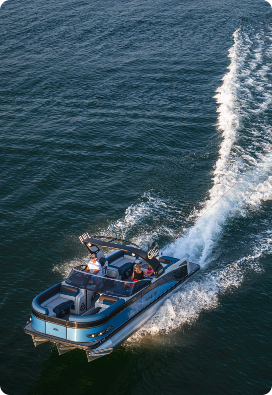 A blue and white motorboat speeds across the water, leaving a trail of wake behind it. Two people are seated in the boat under a sunny sky, enjoying the ride.