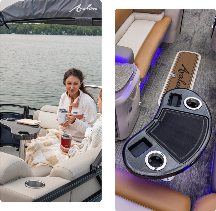 Two people relax on a boat, wrapped in blankets, holding drinks. The boat features plush seating and a multifunctional table with cup holders and storage. The water is calm, and trees line the distant shore.