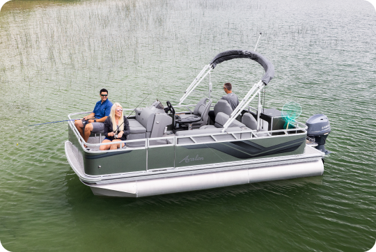 A pontoon boat, from one of the top brands, glides smoothly across the calm lake with three people on board. One is fishing, another is seated, and the third is steering. The sleek gray vessel boasts a canopy and an outboard motor, surrounded by scattered reeds.