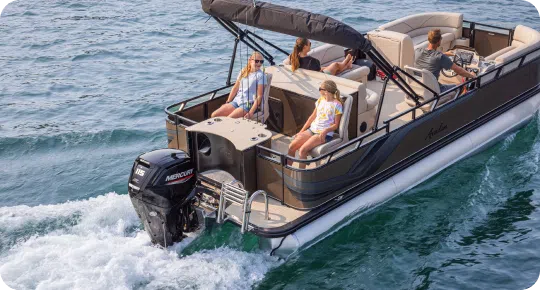 A group of people relax on a pontoon boat with a canopy, cruising on clear blue water. The Mercury engine, a favorite among top pontoon boat brands, is visible at the back, creating a gentle wake as it moves forward.