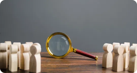 A magnifying glass rests on a wooden table, surrounded by small wooden figurines grouped on either side, evoking the meticulous scrutiny akin to comparing pontoon boat brands.