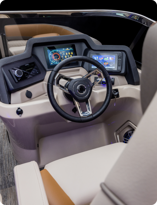 A modern boat dashboard, common among top pontoon boat brands, features a steering wheel, digital control screens, and various controls. The interior is sleek with beige and brown seating, suggesting a luxurious design.