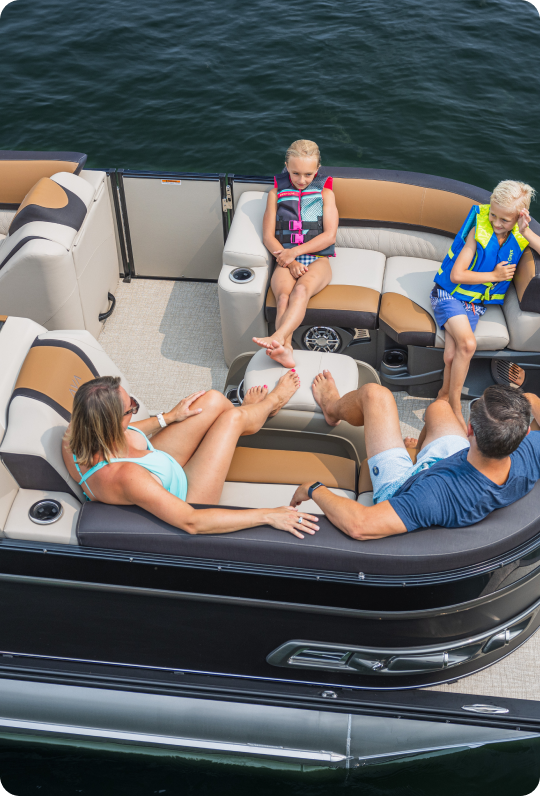 A family of four enjoys a leisurely day on a well-crafted pontoon boat. Two adults sit side by side while the children, safely wearing life jackets, play nearby. The boat glides smoothly across the serene water, showcasing the quality associated with top pontoon boat brands.