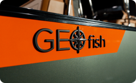 Close-up of a boat with the word "GEOfish" and a compass design on the side, sailing past discussions of pontoon prices. The words stand out against a bold orange stripe on an olive green background.